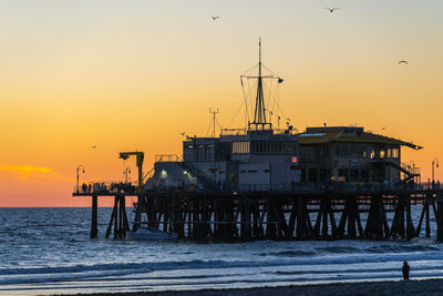 Pier on sea against orange sky