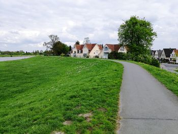 Footpath amidst field and houses against sky