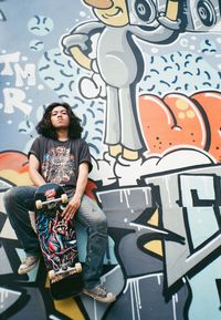 Full length of woman sitting against graffiti wall