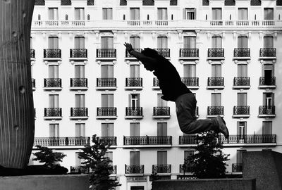 Side view of man jumping against buildings in city