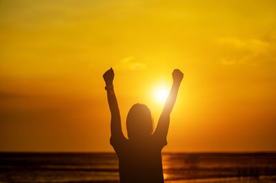 Silhouette person standing by sea against sky during sunset