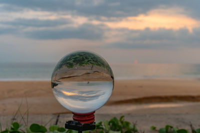 Close-up of glass on beach against sky during sunset