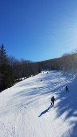 People skiing on snow field against clear blue sky