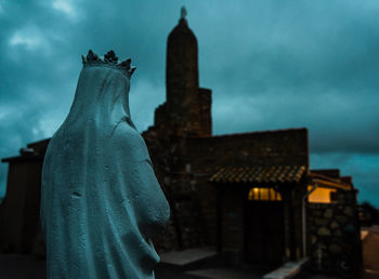 Close-up of statue and church against cloudy sky at dusk