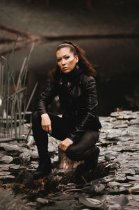 Full length portrait of woman crouching on tree stump in lake