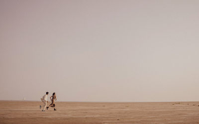 Rear view of woman walking on beach against clear sky