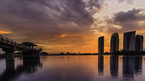 Bridge over river by buildings against sky during sunset