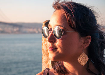 Close-up of young woman wearing sunglasses looking at sea during sunset