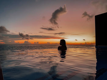 Silhouette naked woman in sea against sky during sunset in the swimming pool of in maldives