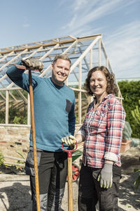 Portrait of happy couple standing with tools at community garden