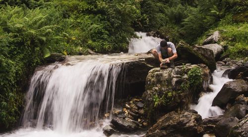 Man crouching by waterfalls in forest