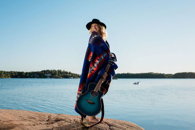 Woman smiling holding her guitar wrapped in pendleton at the beach