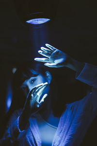 Portrait of young man holding illuminated lighting equipment in dark room