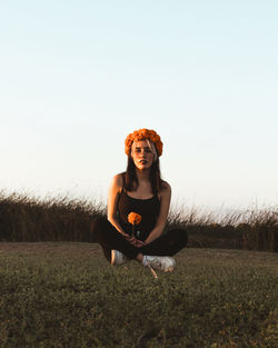 Young woman sitting on field against clear sky