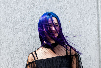 Smiling woman with dyed hair standing against wall