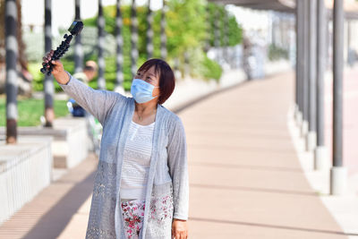 Woman wearing mask vlogging while standing outdoors