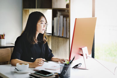 Young woman using mobile phone while sitting on table