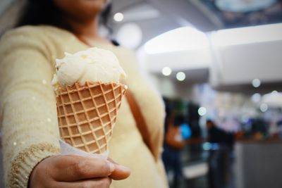 Midsection of woman holding ice cream cone in restaurant