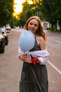 Cute and pretty young girl or student, eats and poses with sugar blue candy cotton on town street