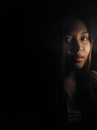 Portrait of young woman against black background