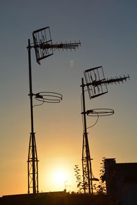 Low angle view of antennas against sky during sunset