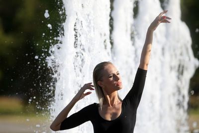 Beautiful woman with hand raised standing against fountain