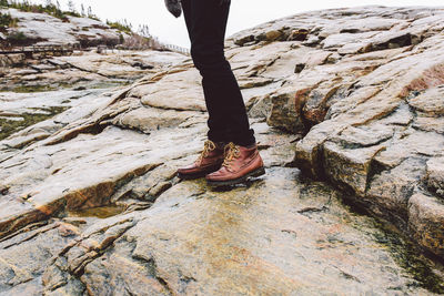 Low section of woman wearing boot standing on rock