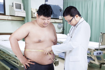 Doctor measuring shirtless male patient waist in hospital