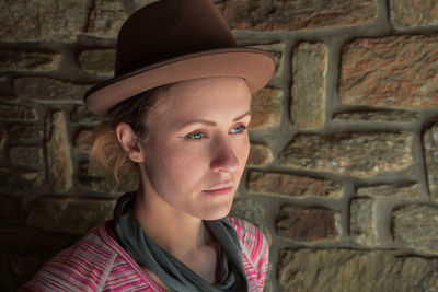 Close-up of woman in hat by brick wall