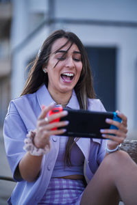 Smiling young woman using mobile phone while sitting on bench outdoors