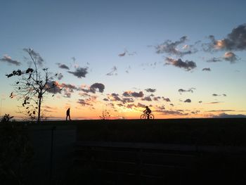 Silhouette people riding bicycle on field against sky during sunset
