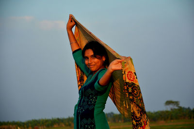 Portrait of smiling young woman standing against sky