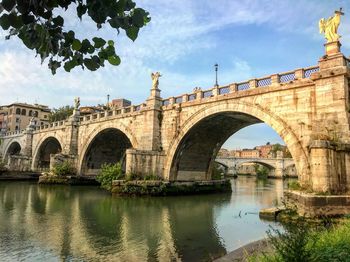 Arch bridge over river against cloudy sky