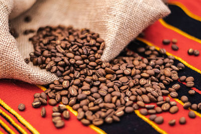 Roasted coffee beans or seeds in a jute sack and scattered on a tablecloth with african decorations