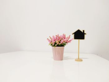 Flowers in pot by blank sign on table against white wall