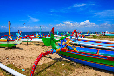 Boats moored on beach against blue sky