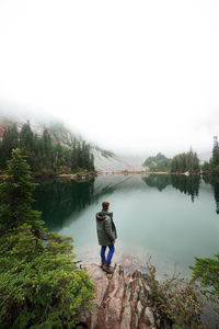 Rear view of man standing by lake against sky