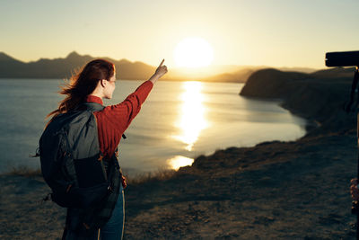 Woman photographing at beach against sky during sunset