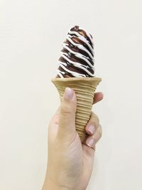 Close-up of hand holding ice cream against white background