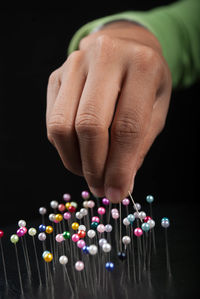 Cropped hand of person with colorful straight pins against black background