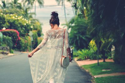 Rear view of woman walking on road along trees