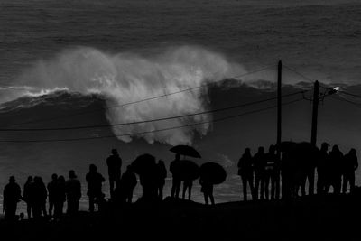 Silhouette people standing by sea against sky