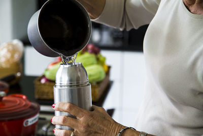 Midsection of senior woman pouring water in insulated drink container