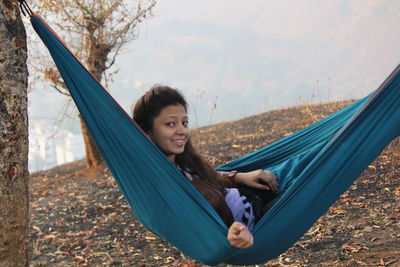 Portrait of smiling young woman sitting against sky