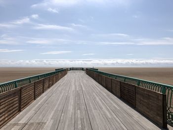 Wooden footbridge on boardwalk against sky