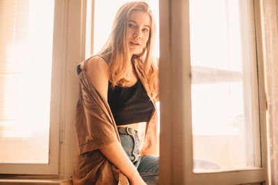 Young woman standing at balcony doorway at home in summer