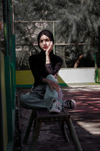 Portrait of young woman sitting against wall