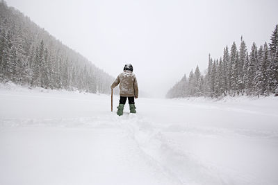 Rear view of man hiking on snow covered field