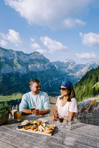 Friends sitting on table by mountains against sky