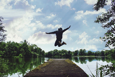 Man jumping in lake against sky